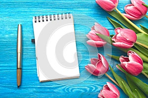 Tulip flowers and blank note pad paper page on wooden background with copy space. Woman day concept. Romantic background.