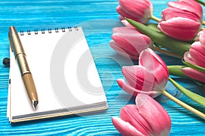 Tulip flowers and blank note pad paper page on wooden background with copy space. Woman day concept. Romantic background.