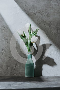 Tulip flowers in blue vase on concrete surface with shadow