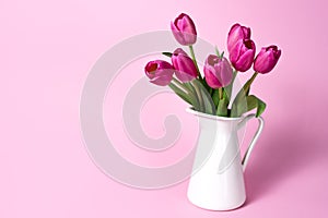 Tulip flowers in a jug on pink background