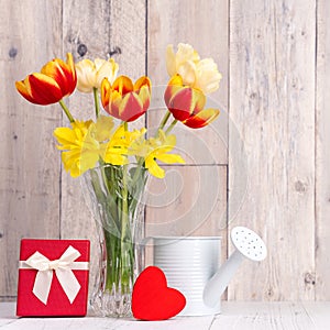 Tulip flowers for Mother`s Day greeting in glass vase over wooden table and wall