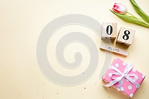 Tulip with a gift and a wooden calendar on a yellow background, place for text, flat lay. March 8, International Women`s Day