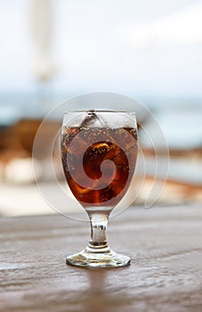 Tulip glass with cola on table. Beach umbrellas on the background