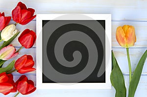 Tulips with blank black chalkboard picture frame on white wooden background. romantic picture.