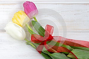 A tulips bouquet with red ribbon on a white wooden background