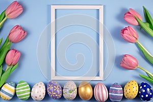 Tulips flowers and Easter eggs with wooden frame on blue background. Card for Happy Easter
