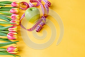 Tulips, green apple and tape measure on yellow background. Concept of spring detox and slimming.