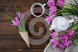 Tulips, a notebook, a white teapot and a cup of tea are laid out on a wooden table