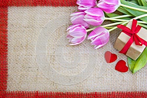 Tulips and two red hearts on brown cloth Background.