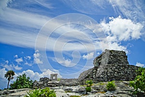 In Tulum an ancient stone tower rises at the top of a mound with an arch standing firm to the left under a blue sky
