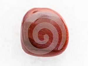 tumbled red goldstone gemstone on white marble