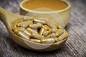 Tumeric capsule and tumeric finely powder in bowl  on wood table.