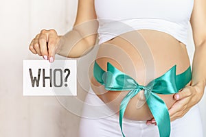 Tummy with green ribbon and bow of pregnant caucasian woman which is holding question