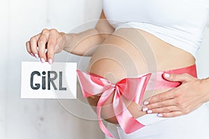 Tummy with pink ribbon and bow of pregnant caucasian woman which is holding nameplate girl