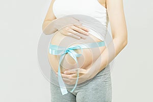 A tummy of a pregnant woman with blue ribbon bow,Pregnancy health care preparing for baby concept.Motherhood among teenage mother