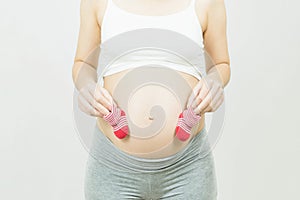 A tummy of a pregnant woman with red baby`s bootees,Pregnancy health care preparing for baby concept.Motherhood among teenage