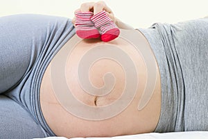 A tummy of a pregnant woman with red baby`s bootees,Pregnancy health care preparing for baby concept.Motherhood among teenage