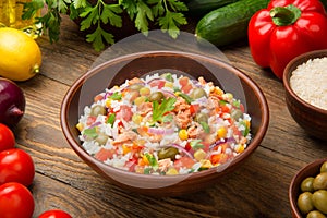 Tuna and rice salad in a terracotta salad bowl on a rustic wooden table with ingredients.