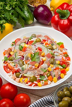 Tuna rice salad in a white porcelain salad bowl on a white rustic wooden table with ingredients.