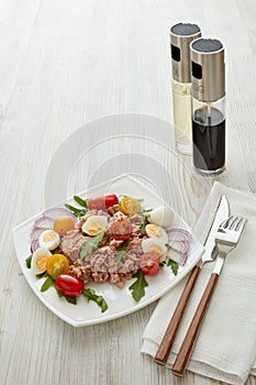 Tuna salad with arugula and tomatoes on light wooden background. Healthy food, seafood menu