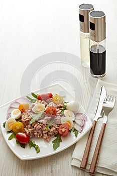 Tuna salad with arugula and tomatoes on light wooden background. Healthy food, seafood menu