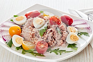 Tuna salad with arugula and tomatoes on light wooden background. Healthy food, seafood menu