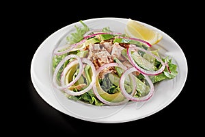 Tuna salad with avocado and arugula on a white plate, on a black background.