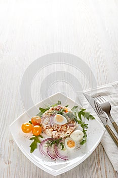 Tuna salad with rice, arugula and tomatoes on light wooden background. Healthy food, seafood menu