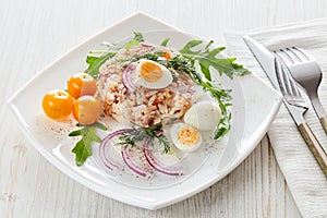 Tuna salad with rice, arugula and tomatoes on light wooden background. Healthy food, seafood menu