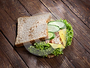 Tuna sandwich with fresh green salad and cucumbers on rustic wooden table surface