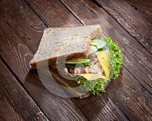 Tuna sandwich with fresh green salad and cucumbers on rustic wooden table surface