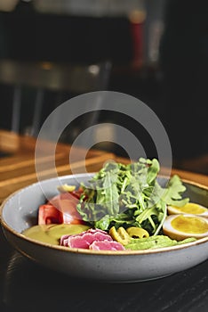 Tuna sashimi with boiled eggs, avocado, fresh tomatoes and arugula in a plate over black background.