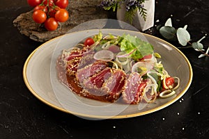 Tuna slices with vegetable salad of cherry tomatoes, radishes, onions, lettuce and adjika tomato sauce. Main fish dish