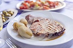 Tuna steak accompanied with potatoes, olives, tomato salad and w