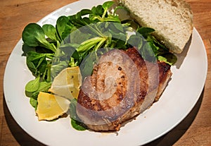 Tuna steak with corn salad, lemons slices and bread on a white p