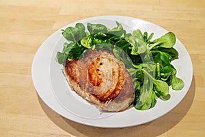 Tuna steak with corn salad on a white plate on a wooden background, close up