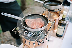 Tuna steak is fried in a frying pan with spices on a gas burner on a table in the garden