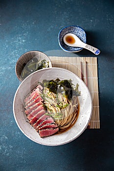 Tuna steak ramen. Japanese soup with noodles ramen, miso, fried tuna steak and seaweed algae. Top view. blue background