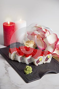 Tuna sushi roll served on black plate, Glass with pink rose flower petals on marble background