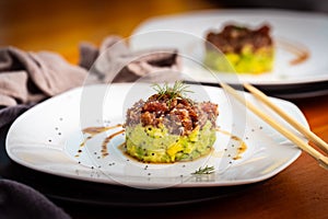 Tuna tartan on white plate served with soja sauce and decorating chopsticks photo