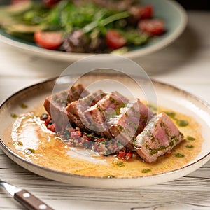 tuna tataki with vegetables and sauce on white plate served on wooden table in restaurant.