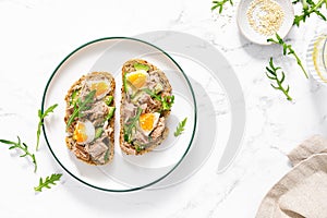 Tuna toast. Open sandwiches with whole grain bread, canned tuna, boiled egg, avocado and arugula. Top view