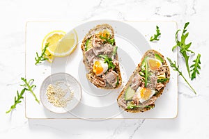 Tuna toast. Open sandwiches with whole grain bread, canned tuna, boiled egg, avocado and arugula. Top view