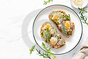 Tuna toast. Open sandwiches with whole grain bread, canned tuna, boiled egg, avocado and arugula. Top view