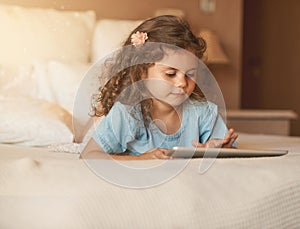 In tune with technology at a young age. an adorable little girl at home lying on her bed playing with a tablet.