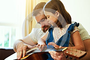 Tuning into a developing talent. an adorable little girl playing the guitar with her father at home.