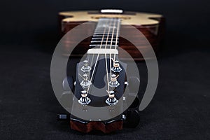 Tuning pegs on wooden machine head of six strings acoustic guitar neck on black background