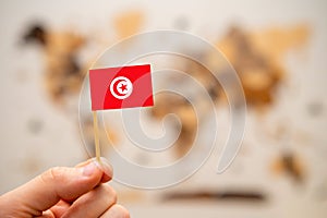 Tunisia flag in mans hand on the world map background.