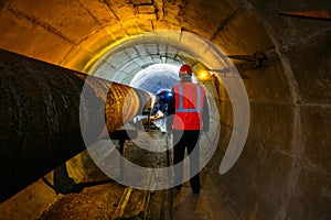 Tunnel worker examines pipeline in underground tunnel photo