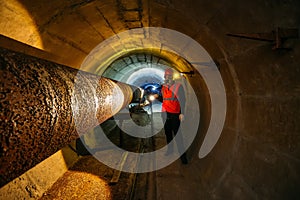 Tunnel worker examines pipeline in underground tunnel